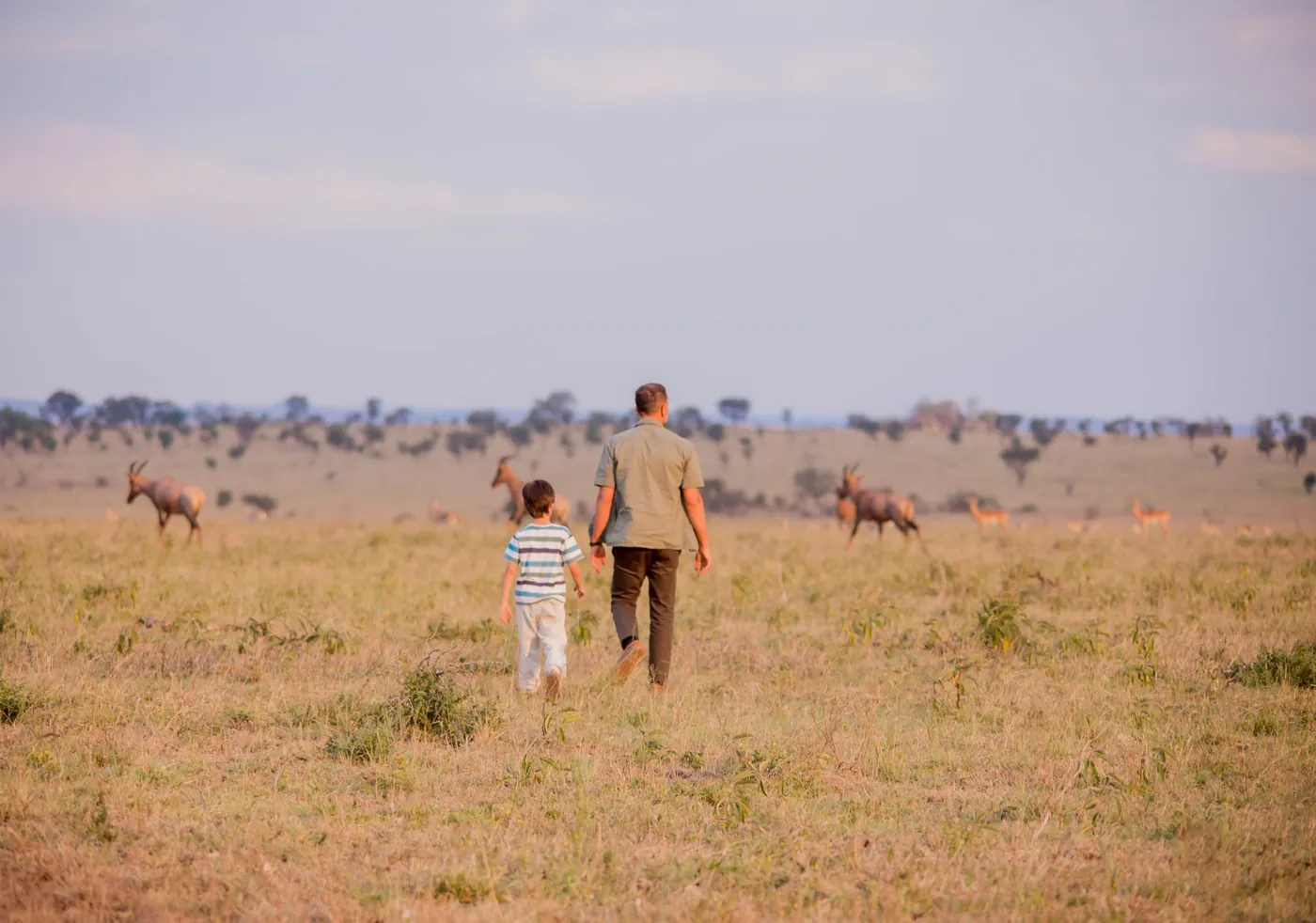 An adult and child walking through a Tanzanian wildlife landscape.